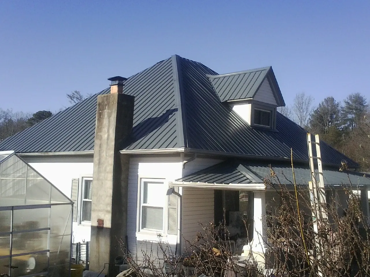 Dark blue standing seam metal roof on a white farmhouse with dormer — Slate & Tile Roof Repair by Roofing Brothers in Bremo Bluff