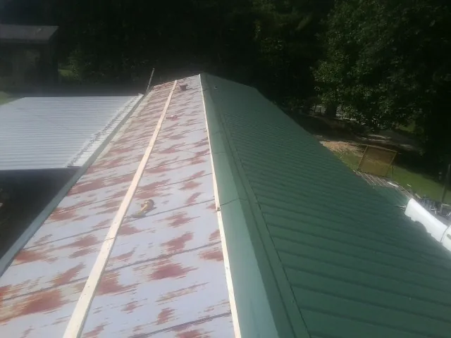 Old rusted panels beside newly installed green metal roofing — Wind Damage Roof Repair by Roofing Brothers in Bremo Bluff