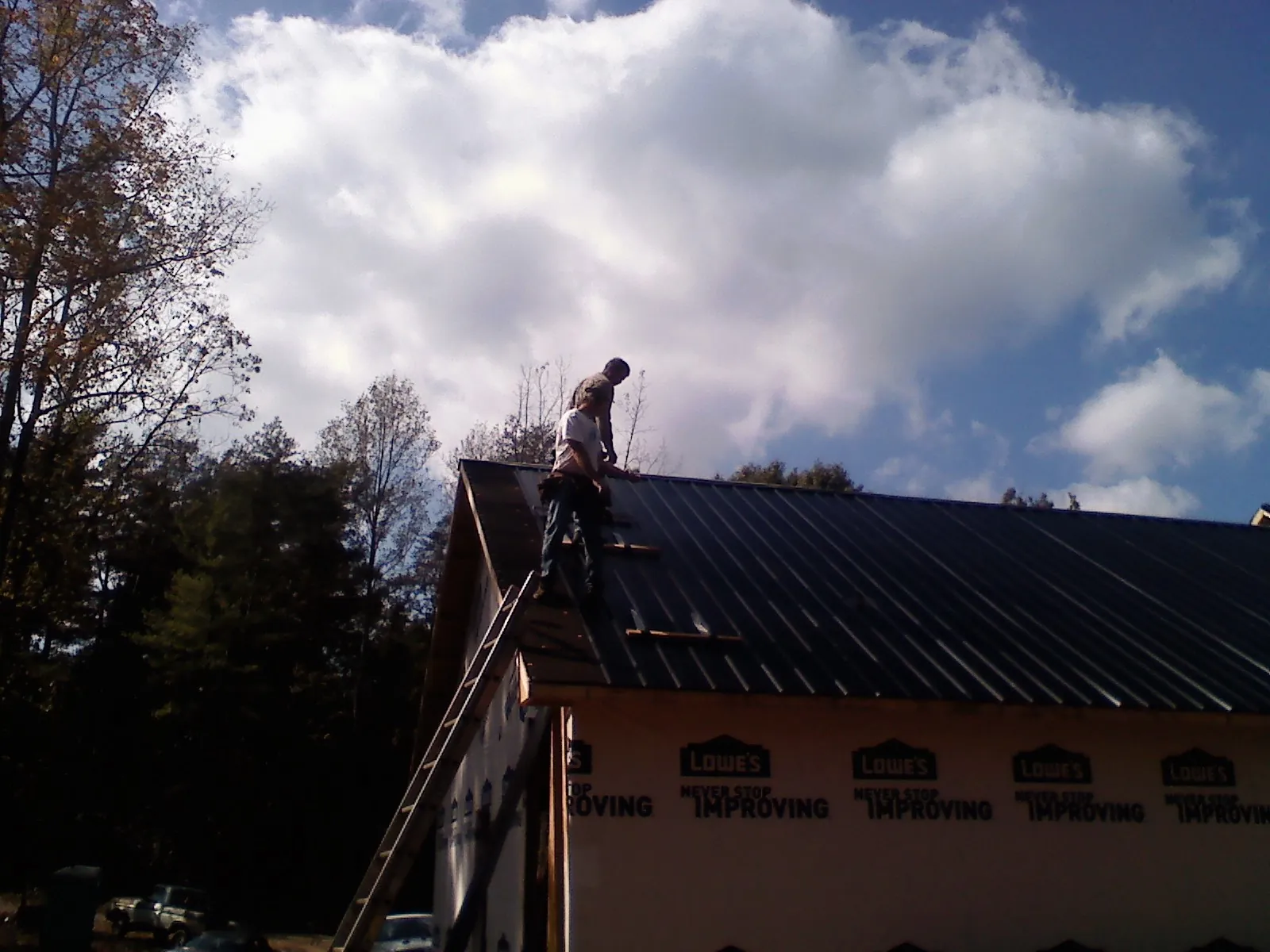 Roofer fastening dark metal panels high against a cloudy sky, from a Roof Inspection job in Bremo Bluff